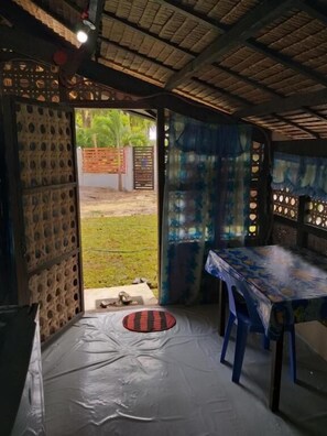 Um quarto com telhado de palha, uma mesa com toalha e uma cadeira azul.