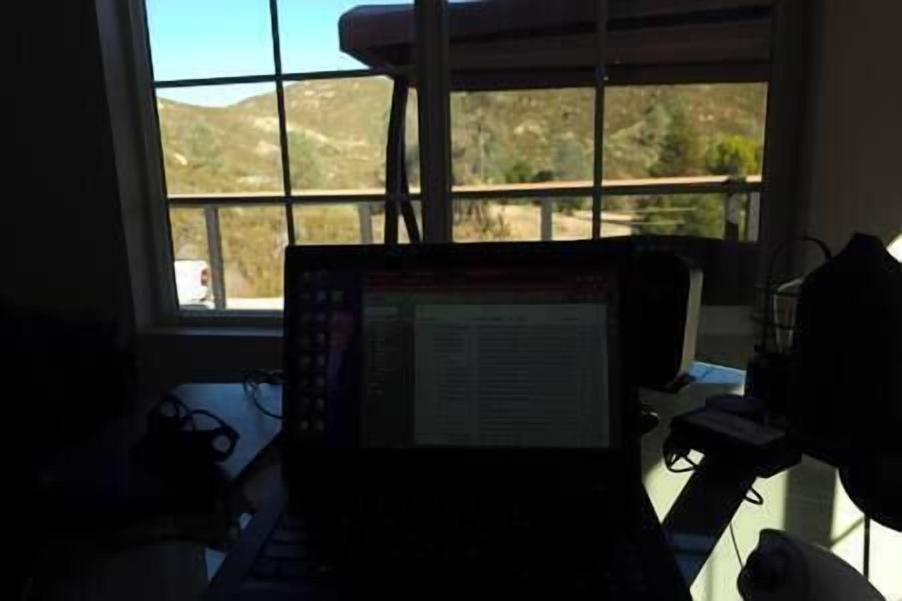 A laptop on a desk with a window view of a landscape.