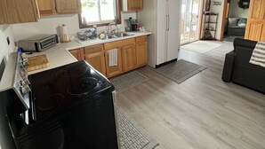 Une cuisine spacieuse avec des meubles en bois, un poêle noir et un réfrigérateur blanc. On y trouve également un coin repas avec un canapé noir et un ventilateur de plafond.