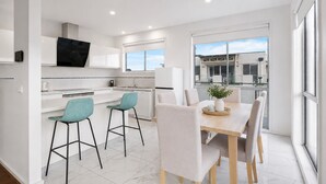Una cocina moderna con armarios blancos, un televisor de pantalla plana y una zona de comedor con mesa y sillas de madera.