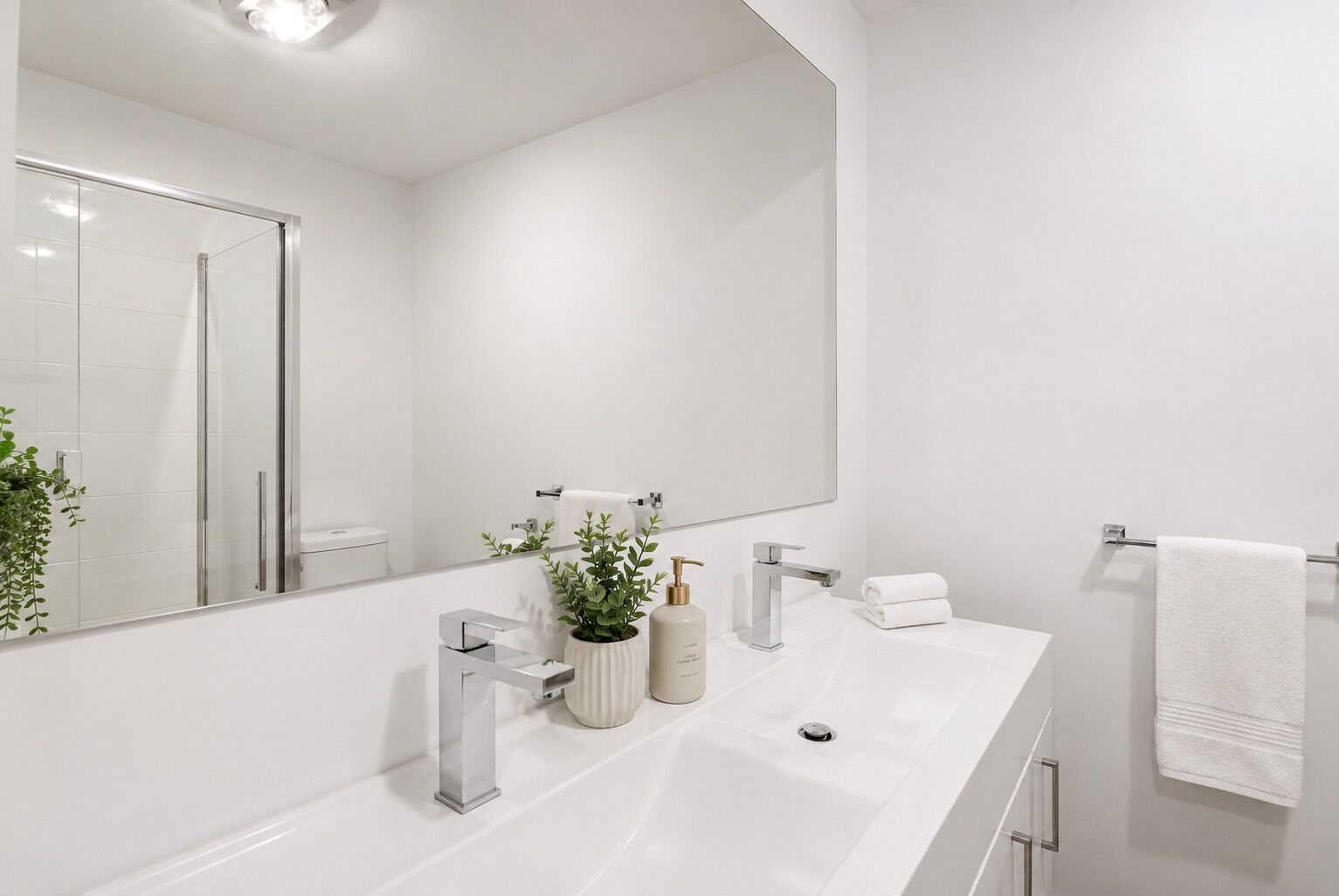 A modern bathroom with a large mirror, two sinks, a towel rack, and a potted plant.