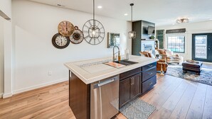A modern kitchen with a central island, stainless steel appliances, and decorative wall clocks. - Stellar Craig Apartment - Walk to Restaurants! (Craig)