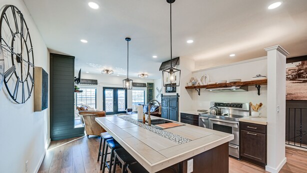 A modern kitchen with a large island, pendant lights, and a clock on the wall. - Stellar Craig Apartment - Walk to Restaurants! (Craig)