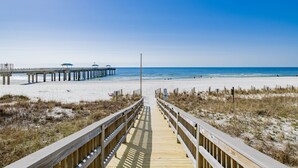 A wooden boardwalk leading to a beach with a pier in the background.