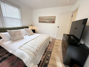 A bedroom with a bed, a TV, a nightstand, a lamp, and a door.