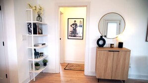Ein Korridor mit Holzboden, weißen Wänden, einer weißen Tür, einem Holzschrank, einem Spiegel und einem gerahmten Bild an der Wand.