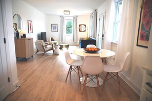 A modern living room with a dining area, wooden flooring, and a view of the outdoors.