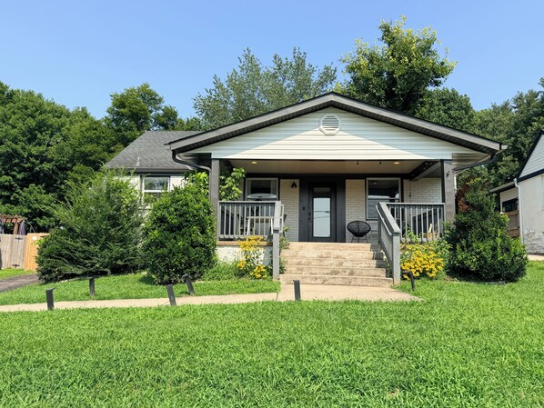 A single-story house with a front porch, a small garden with yellow flowers, and a wooden fence.