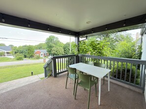 A covered outdoor area with a table and chairs, a railing, and a view of a road and greenery.