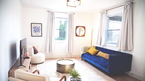 Ein Wohnzimmer mit blauem Sofa, einem weißen Sessel, einem runden Couchtisch und einem Flachbildfernseher.