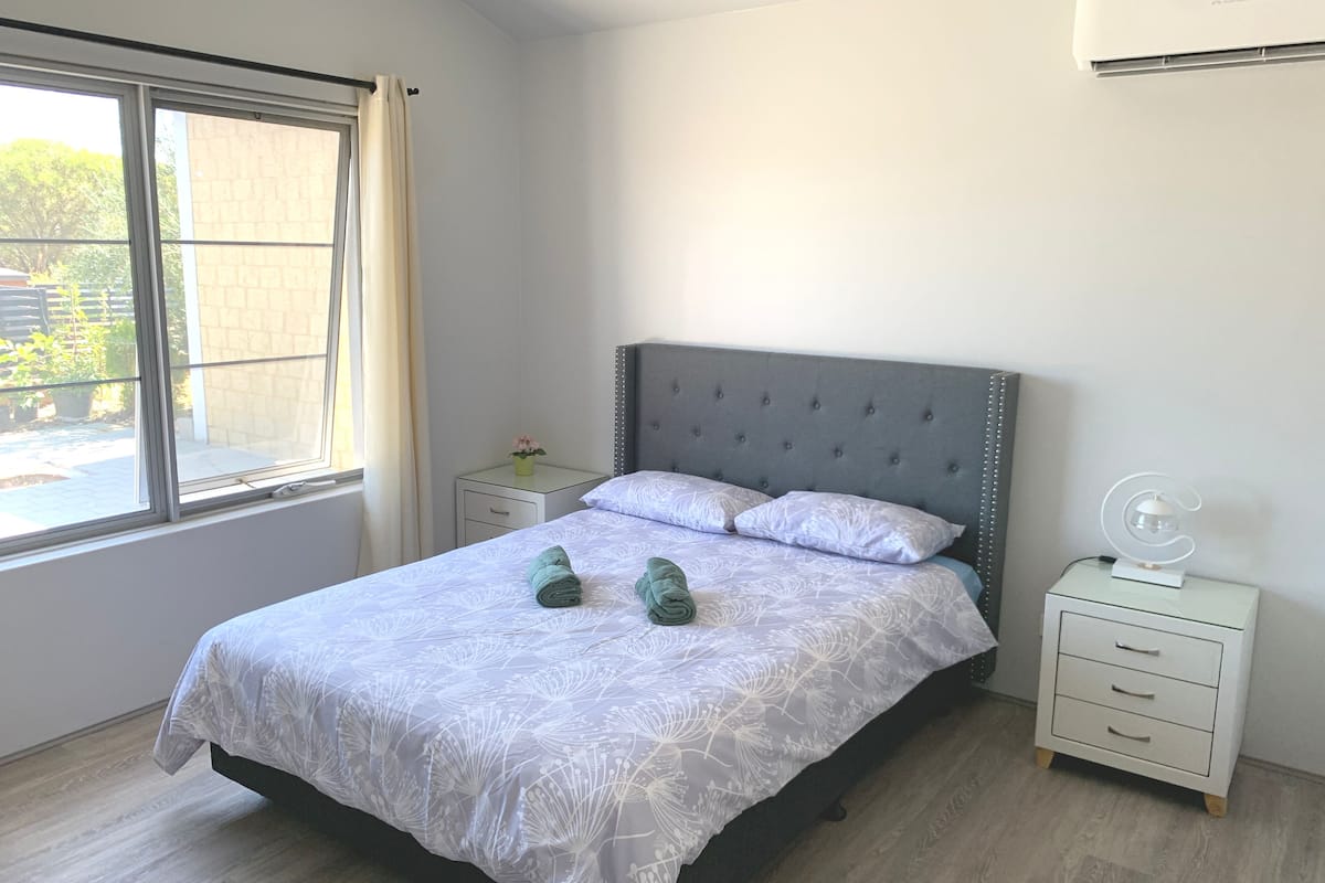 Un dormitorio con cama, mesita de noche, lámpara y ventana.