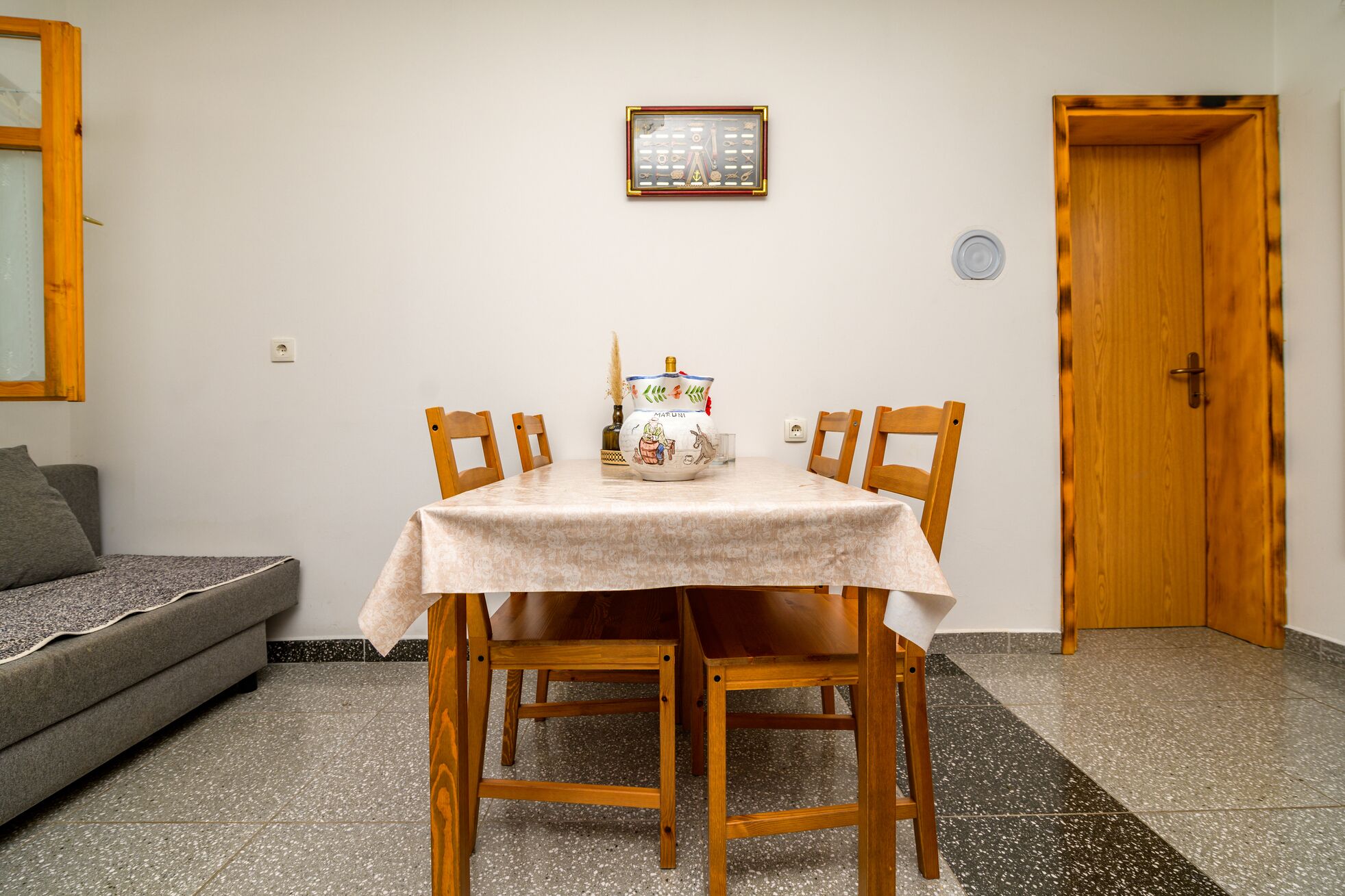 A dining area with a table set for four, wooden chairs, a decorative vase, and a framed picture on the wall.