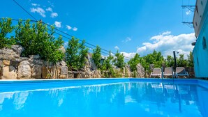 A swimming pool with clear blue water, surrounded by stone walls and greenery. There are lounge chairs and a building with a blue awning. - Villa Plovanija (Kvarner - Poljica) (Poljica)