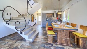 A modern kitchen with a dining area, featuring a wooden table and benches, a staircase with metal railings, and a view of the adjacent living space. - Villa Imperia 3 (Kvarner - Vrh) (Vrh)