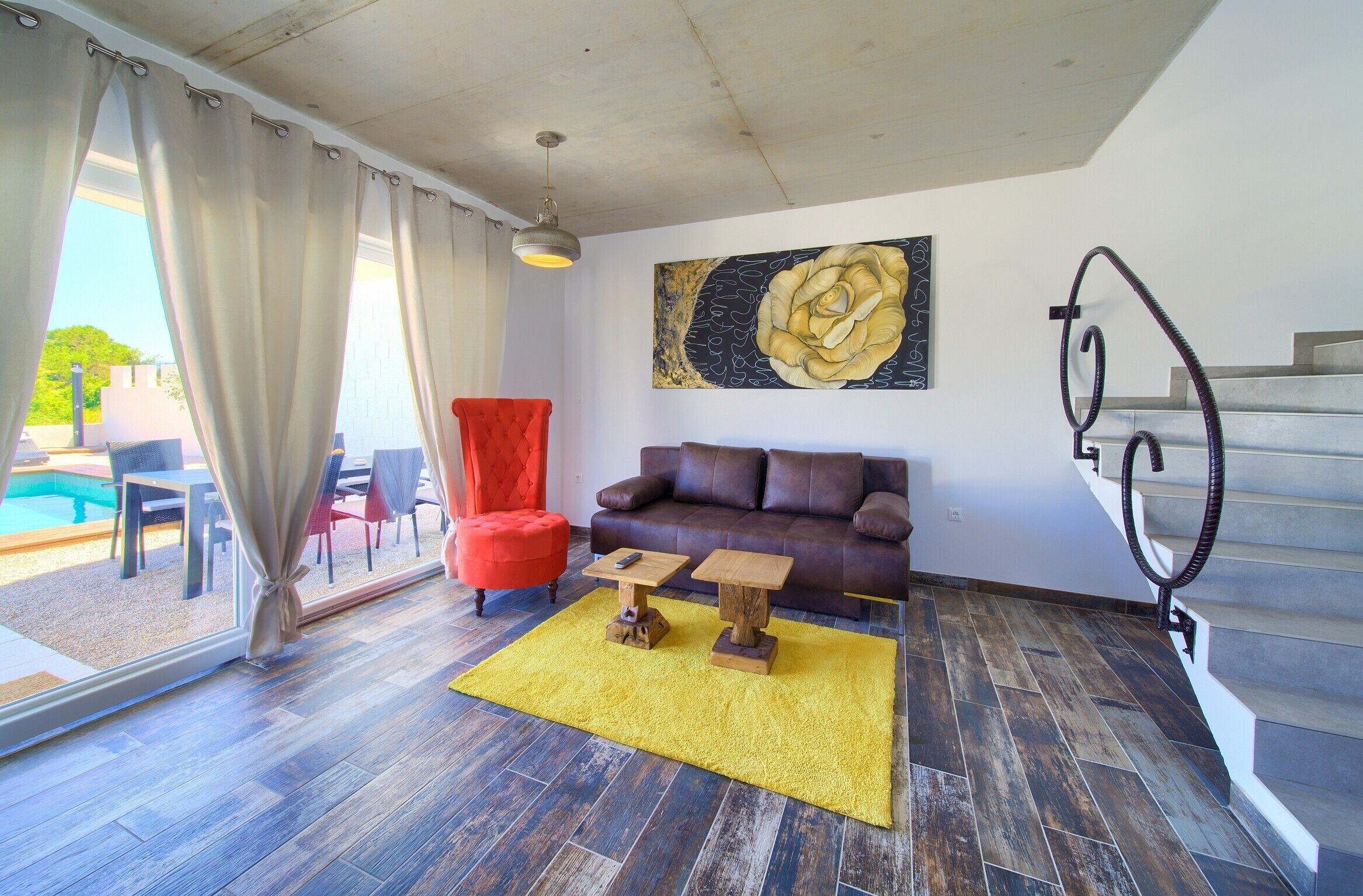 Un salon avec un canapé en cuir marron, un tapis jaune, un fauteuil rouge et un escalier.