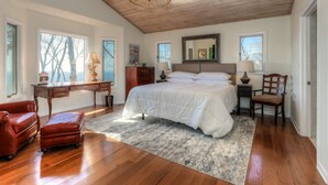 Une chambre à coucher avec un grand lit, un plancher en bois, un bureau, une chaise et un lustre.