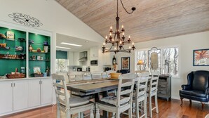 Un coin repas avec une table et des chaises en bois, un lustre et une étagère verte contenant des ustensiles de cuisine.