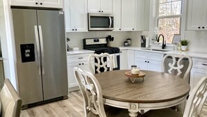 Una cocina con armarios blancos, electrodomésticos de acero inoxidable y una mesa de comedor de madera con sillas.