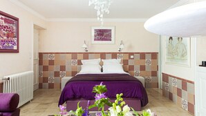 A hotel room with a checkered headboard, a bed with a purple bedspread, a white radiator, a purple bench, and a floral arrangement on the floor. - Bed & Breakfast in the town center (La Rochelle)