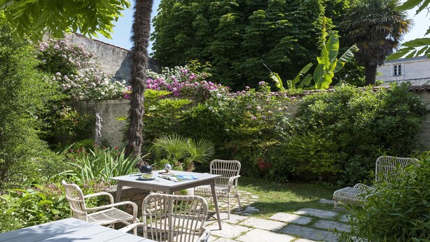 A garden patio with a table and chairs, surrounded by lush greenery and flowering plants. - Bed & Breakfast in the town center (La Rochelle)