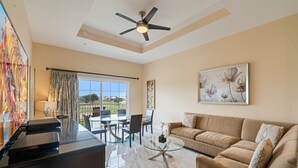 A spacious living room with a beige sofa, a glass coffee table, and a ceiling fan.