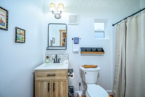 Un baño con tocador de madera, espejo, inodoro y cortina de ducha.