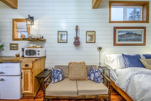 Una habitación acogedora con cama, sofá, un armario de madera, microondas y una guitarra.