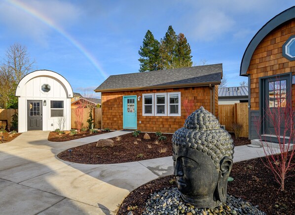 Una casa con puerta azul, un pequeño jardín con una estatua de Buda y una valla de madera.