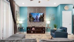 Un salon avec un téléviseur à écran plat fixé à un mur texturé, un fauteuil bleu, un canapé gris et un tapis à motifs.