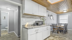 A modern kitchen with white cabinets, a granite countertop, a microwave, and a dining area with a wooden table and chairs. - Mid-Landing Inn (Colorado Springs)