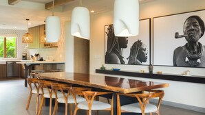 Une cuisine moderne dotée d’un grand îlot central en bois, de luminaires suspendus et d’œuvres d’art accrochées aux murs.