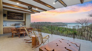 A spacious balcony with a view of a sunset over a valley, wooden furniture, and a modern kitchen area. - As Seen on CBS's Staycation•Resort & Beach Club Access•Concierge•Papagayo Luxury (Peninsula papagayo)
