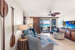 A living room with a view of the ocean, a ceiling fan, and a bar area.