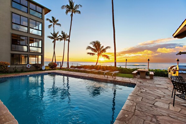 A swimming pool with a sunset view, palm trees, and a building with large windows.