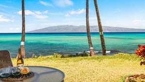 A table with a bottle and glasses, palm trees, and a view of the ocean and mountains. - Luxury meets space in this Premium 1bd Oceanfront (Lahaina)