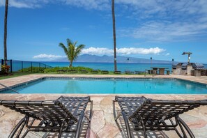 A pool with lounge chairs and a view of the ocean and mountains.