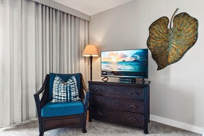 A room with a television displaying a scenic view, a chair with patterned cushions, a lamp, and a decorative leaf on the wall. - Ocean views and A/C combine in this Deluxe studio (Lahaina)