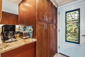 A kitchen with wooden cabinets, a coffee maker, a toaster, and a window with blinds.