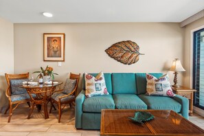 A living room with a sofa, chairs, a table, and a decorative leaf on the wall.