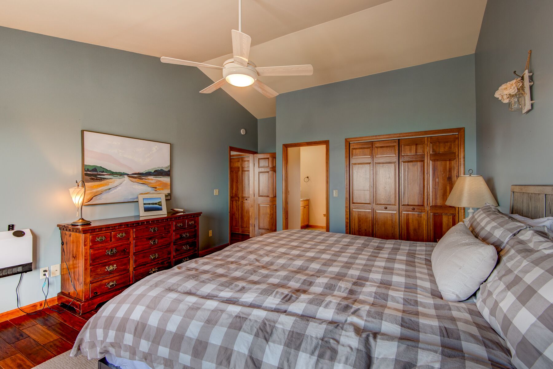 Ein Schlafzimmer mit Bett, Schminktisch, Deckenventilator und einem Bild an der Wand.
