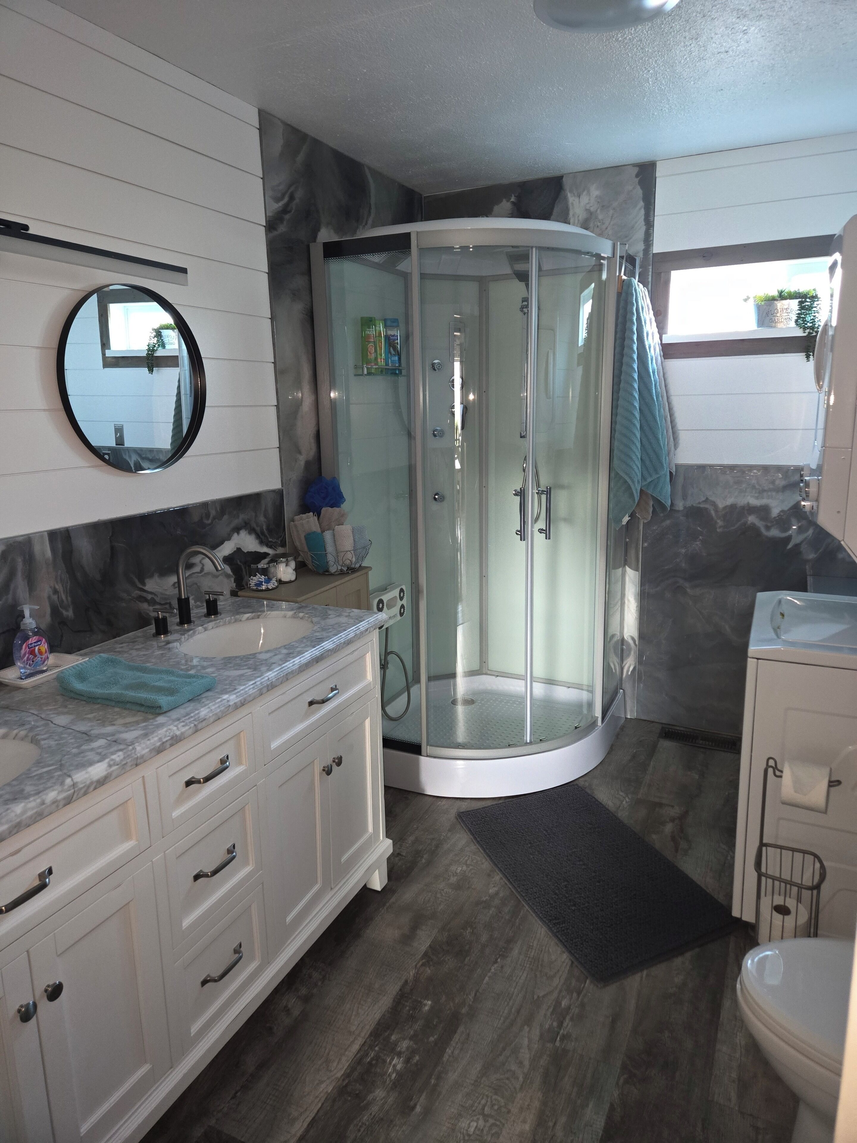 Un baño con cabina de ducha curva, espejo redondo y tocador con encimera de mármol.