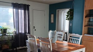 A dining area with a wooden table and white chairs, a ceiling fan, and a view of the outdoors through a window with curtains. - The Shopkeeper's Inn. 
Unique property with history, In the heart of Ely, Nv. (Ely)