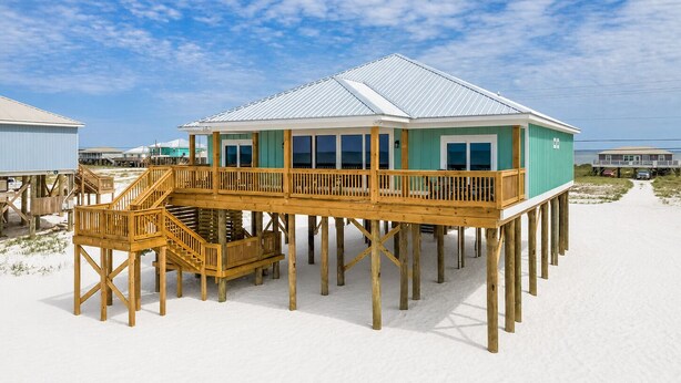 Une maison située en bord de mer, dotée d’une terrasse en bois et de nombreuses fenêtres.
