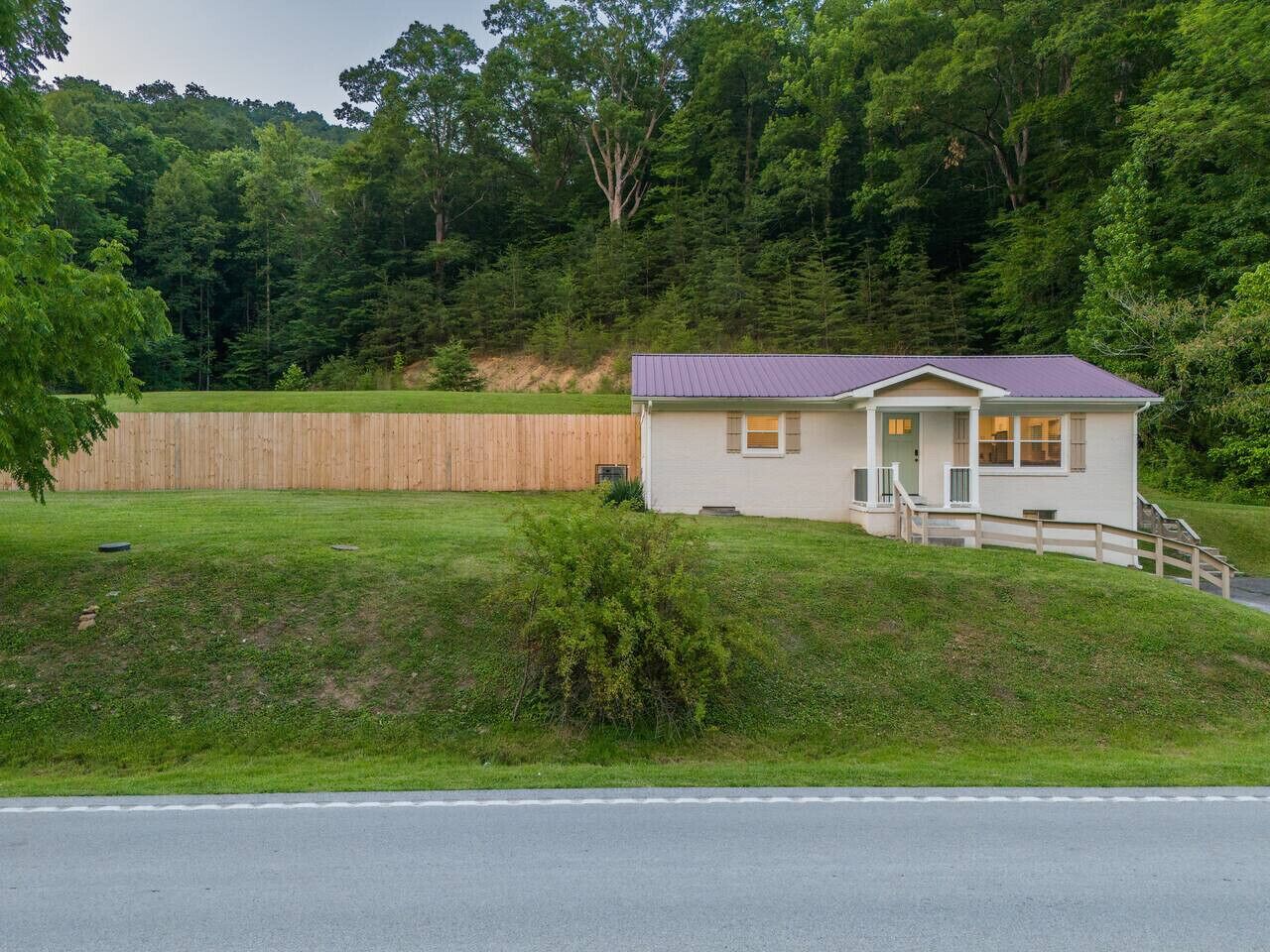A small, single-story house with a sloped roof, a front porch, and a wooden fence in the background.