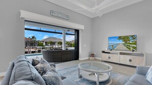 A spacious living room with a large window, a round coffee table, and a TV on a wooden cabinet.