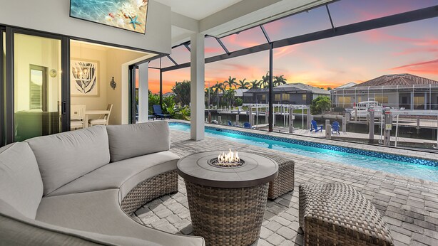 A modern outdoor living area with a pool, a fire pit, and a view of the sunset.