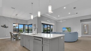 A modern kitchen with a large island, pendant lighting, and a view of the outdoors.