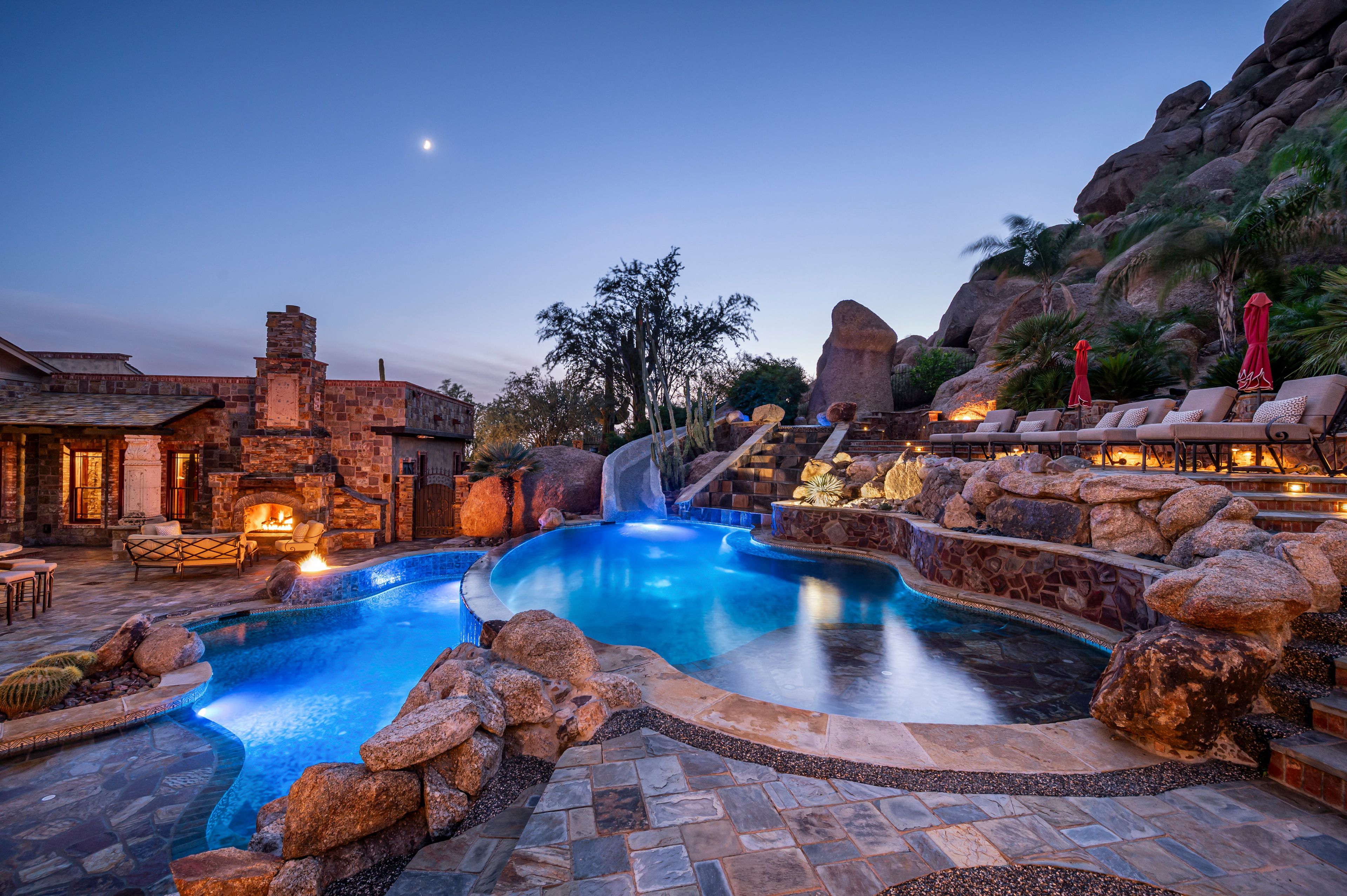 Zona de piscina amb cascada, arquitectura de pedra i mobiliari exterior.