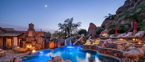 A pool area with a waterfall feature, stone architecture, and outdoor seating.
