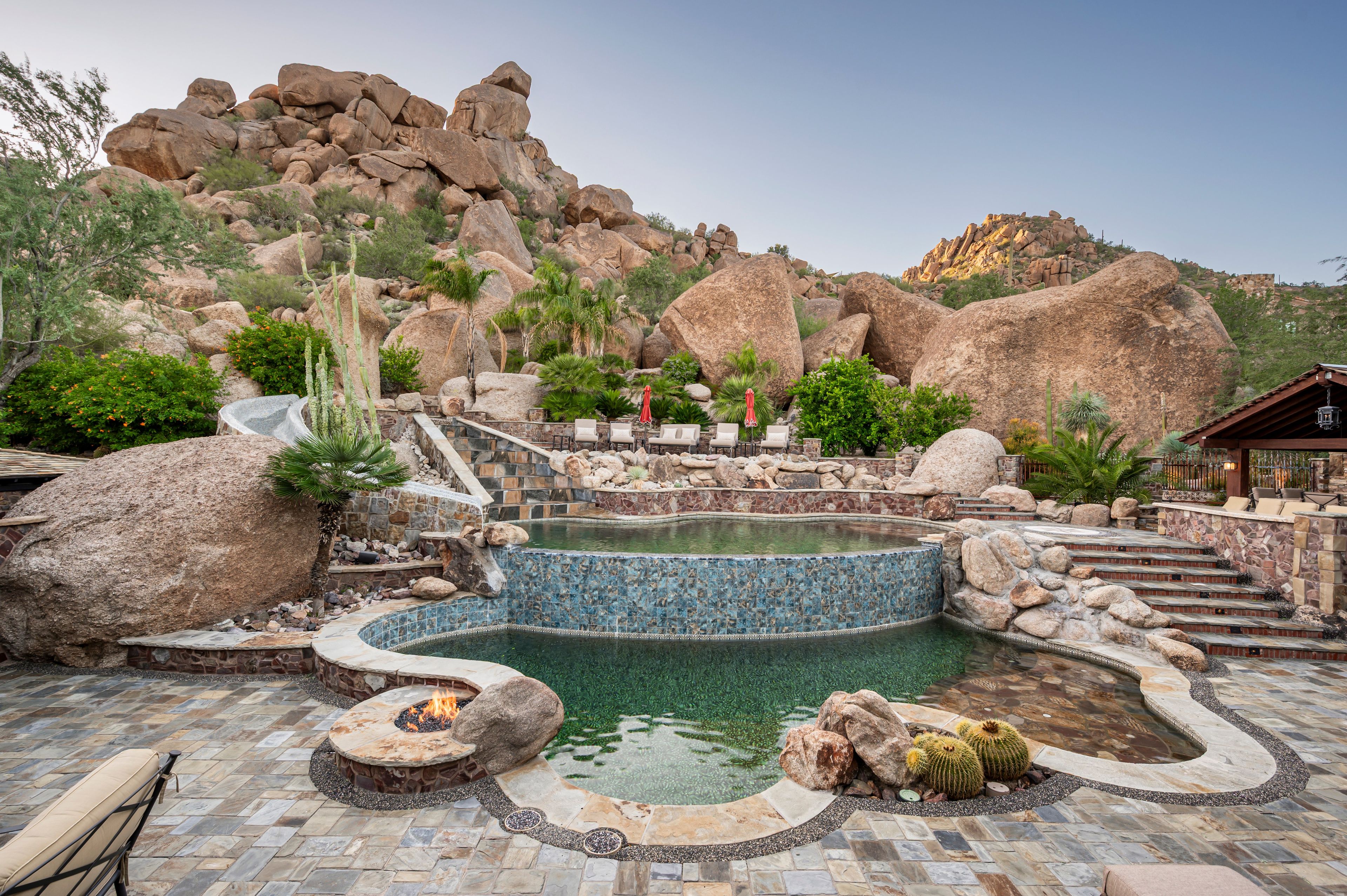 A pool area with a fire pit, seating, and a view of rocky terrain.